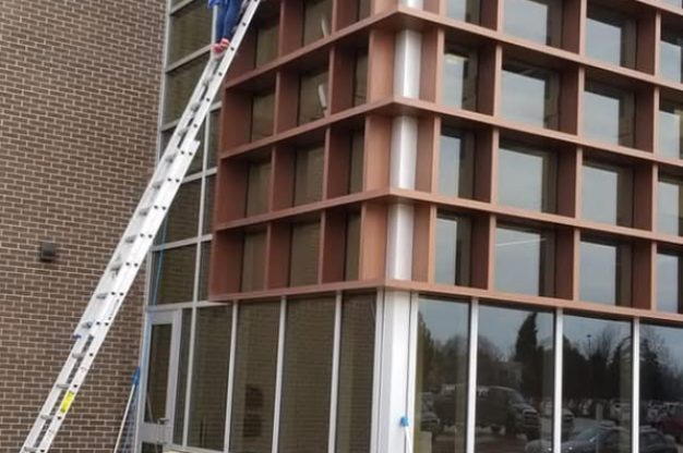 Flo on a ladder cleaning commercial windows